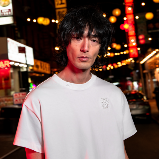 EMB. TEE in white — worn, close-up of tonal embroidered chest emblem and neck branding