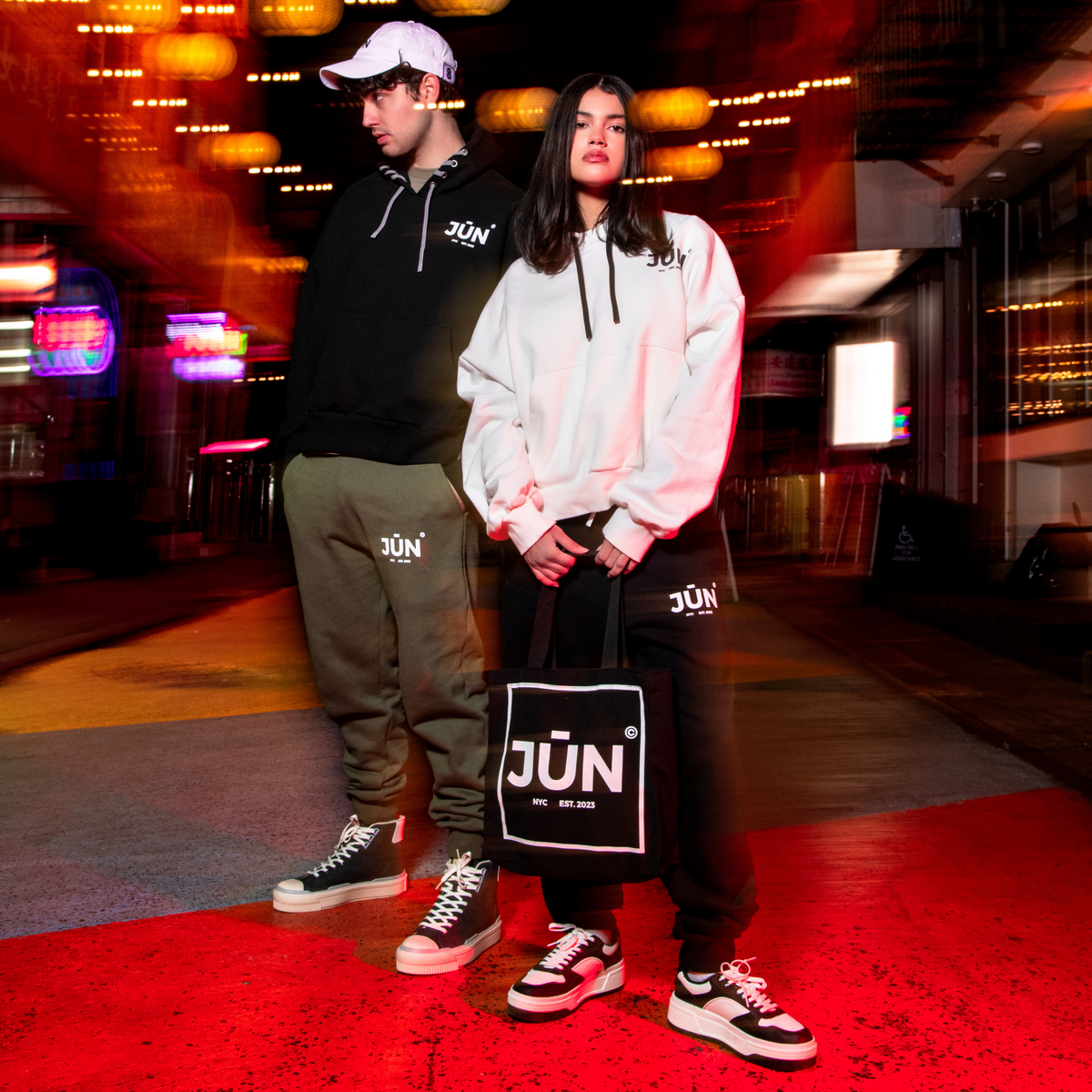 DAWN. SWEATS — lifestyle, two models in motion blur styled with JŪN hoodies and a JŪN tote